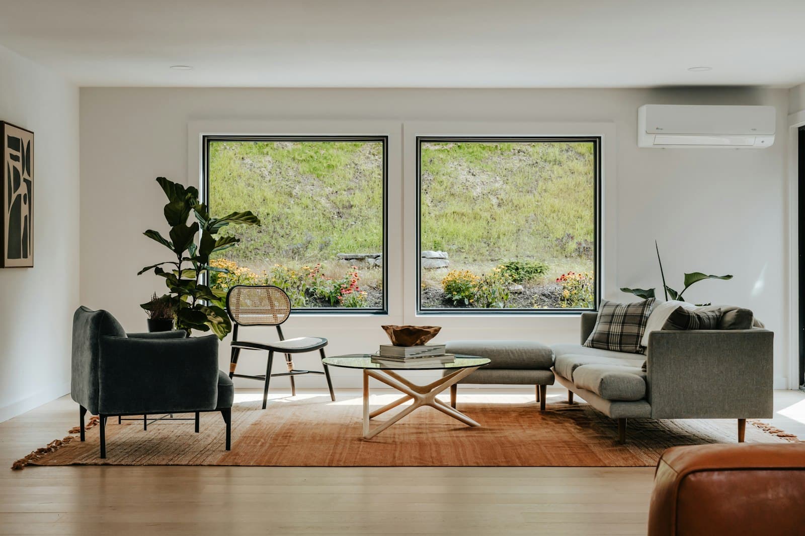 A bright, sunlit living room with two large windows and a green garden view