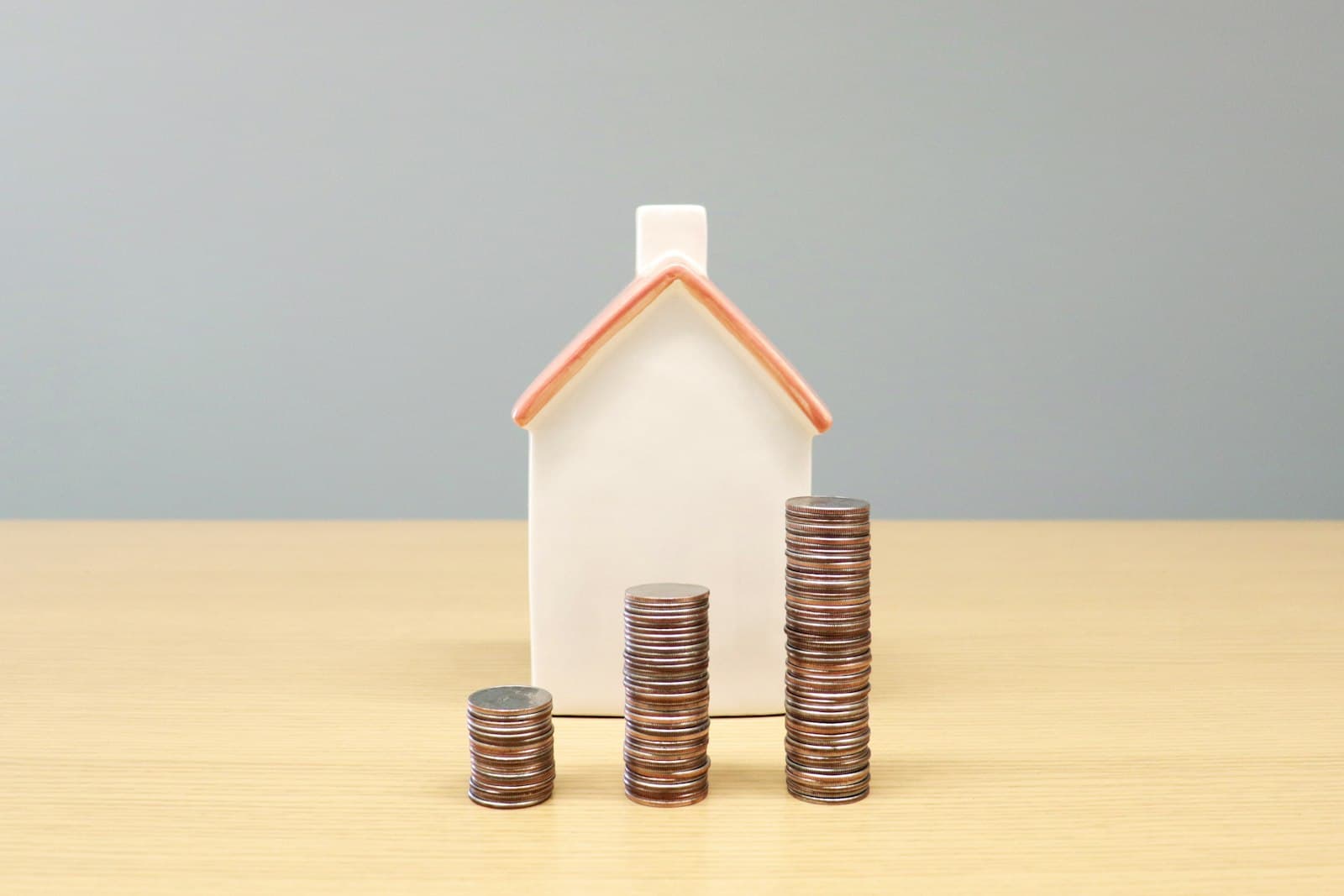 A model house behind three rising stacks of coins