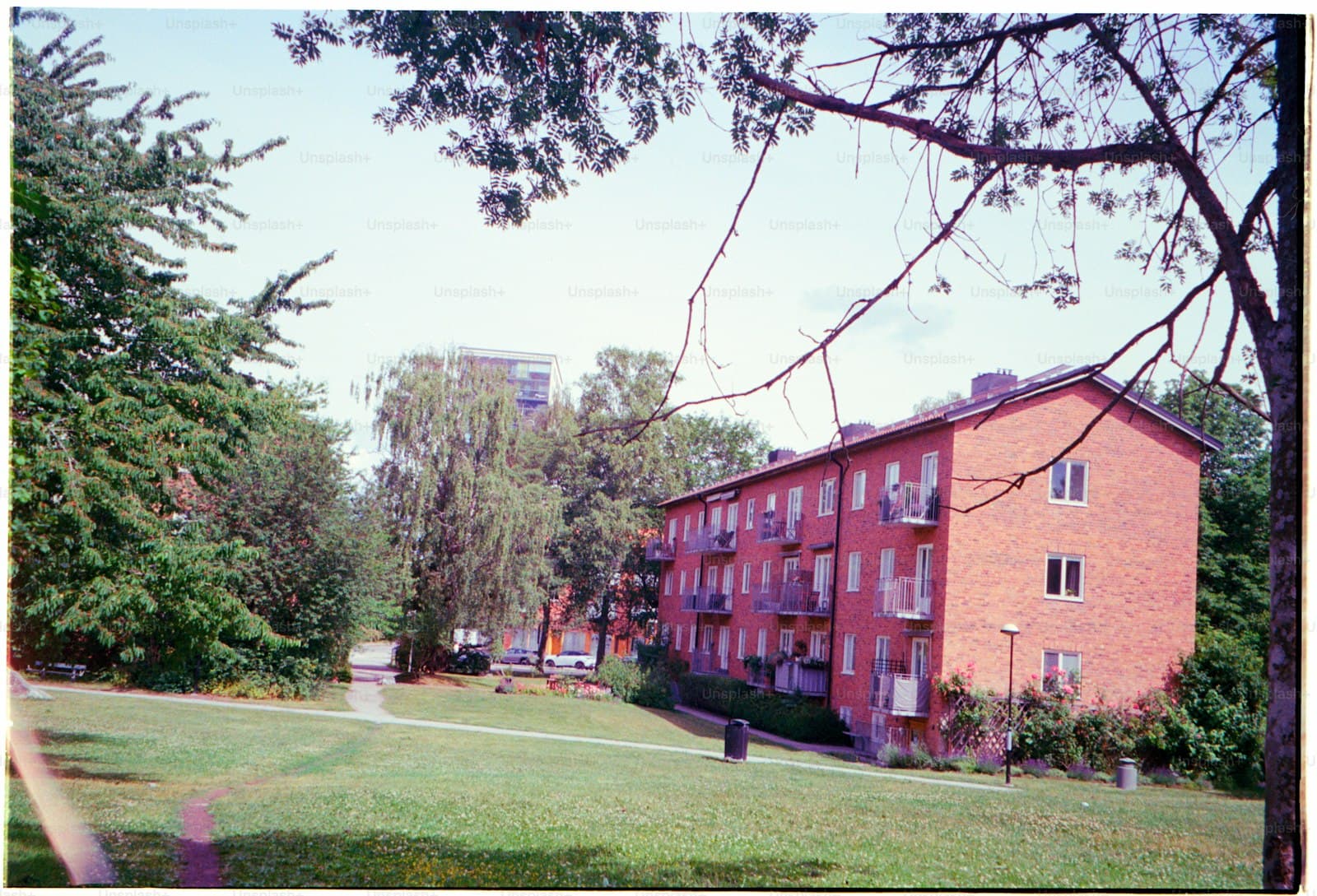 A brick apartment building beside green space under a bright sky