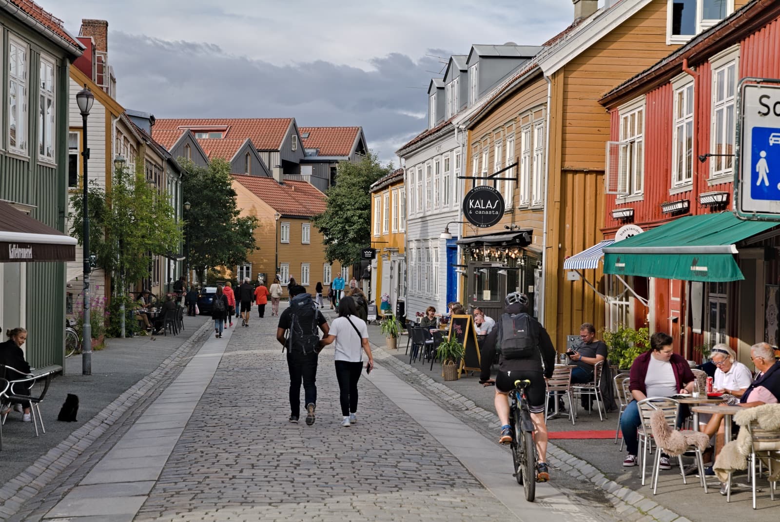 Cobbled Nedre Bakklandet lined with painted wooden houses, cafés and outdoor tables, Bakklandet, Trondheim, Norway.