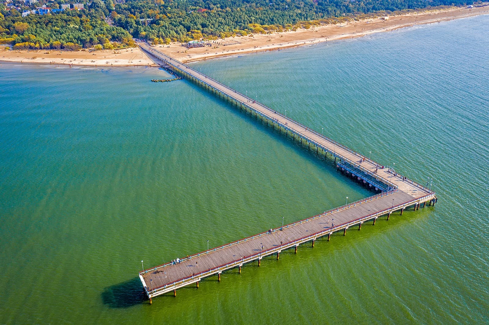 Aerial view of the long Palanga pier stretching into the Baltic Sea, with the sandy beach and pine forest behind