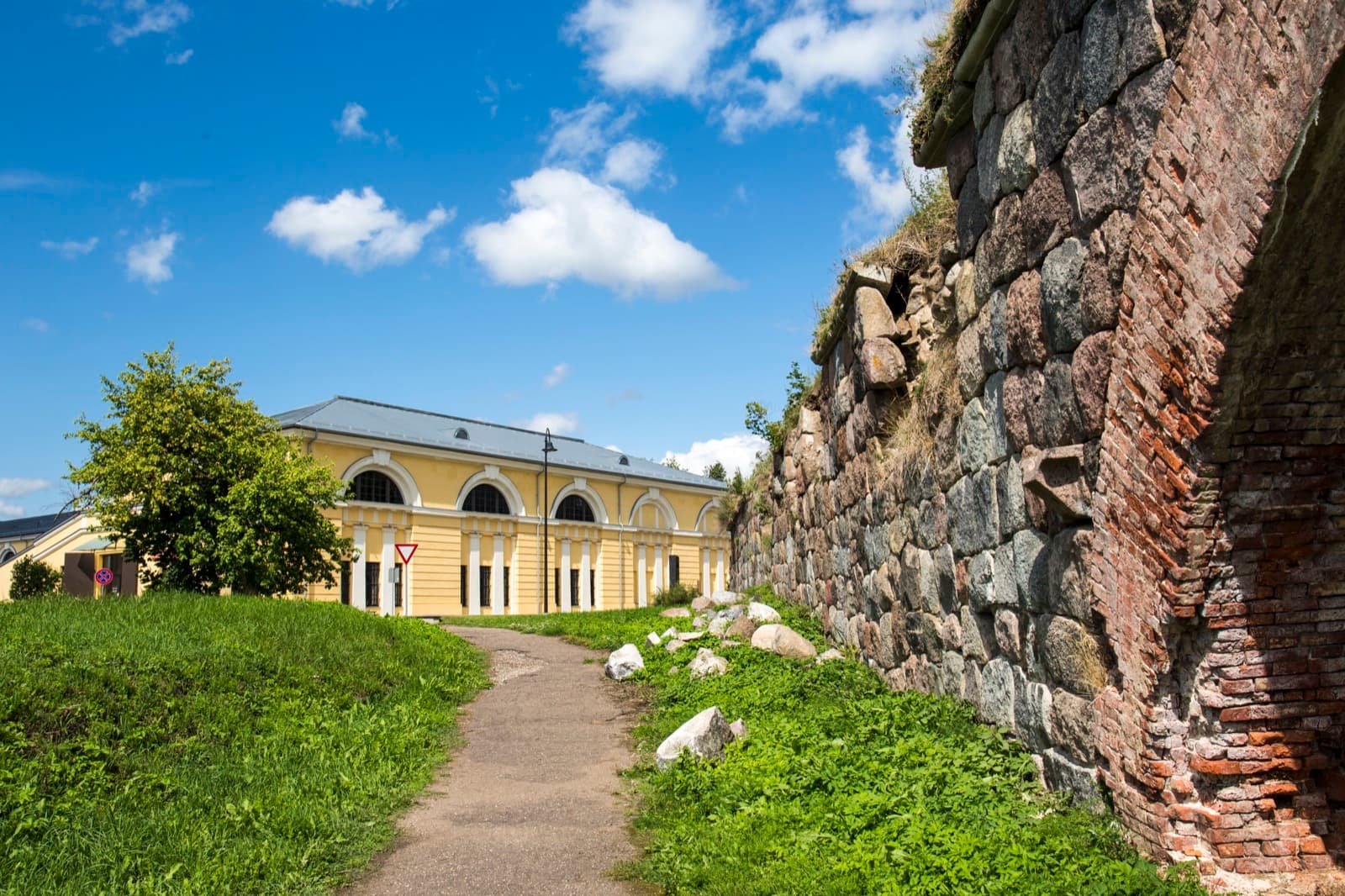 A stone and brick rampart of the Daugavpils Fortress beside one of its restored yellow arsenal buildings, Latvia.