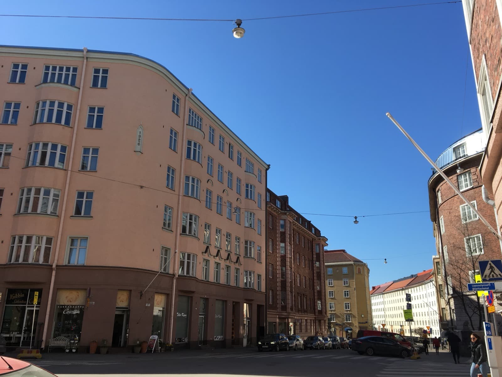 The curving pink 1920s apartment facade on Museokatu in Etu-Töölö, Helsinki, with a flower shop and café at street level under a clear blue sky.