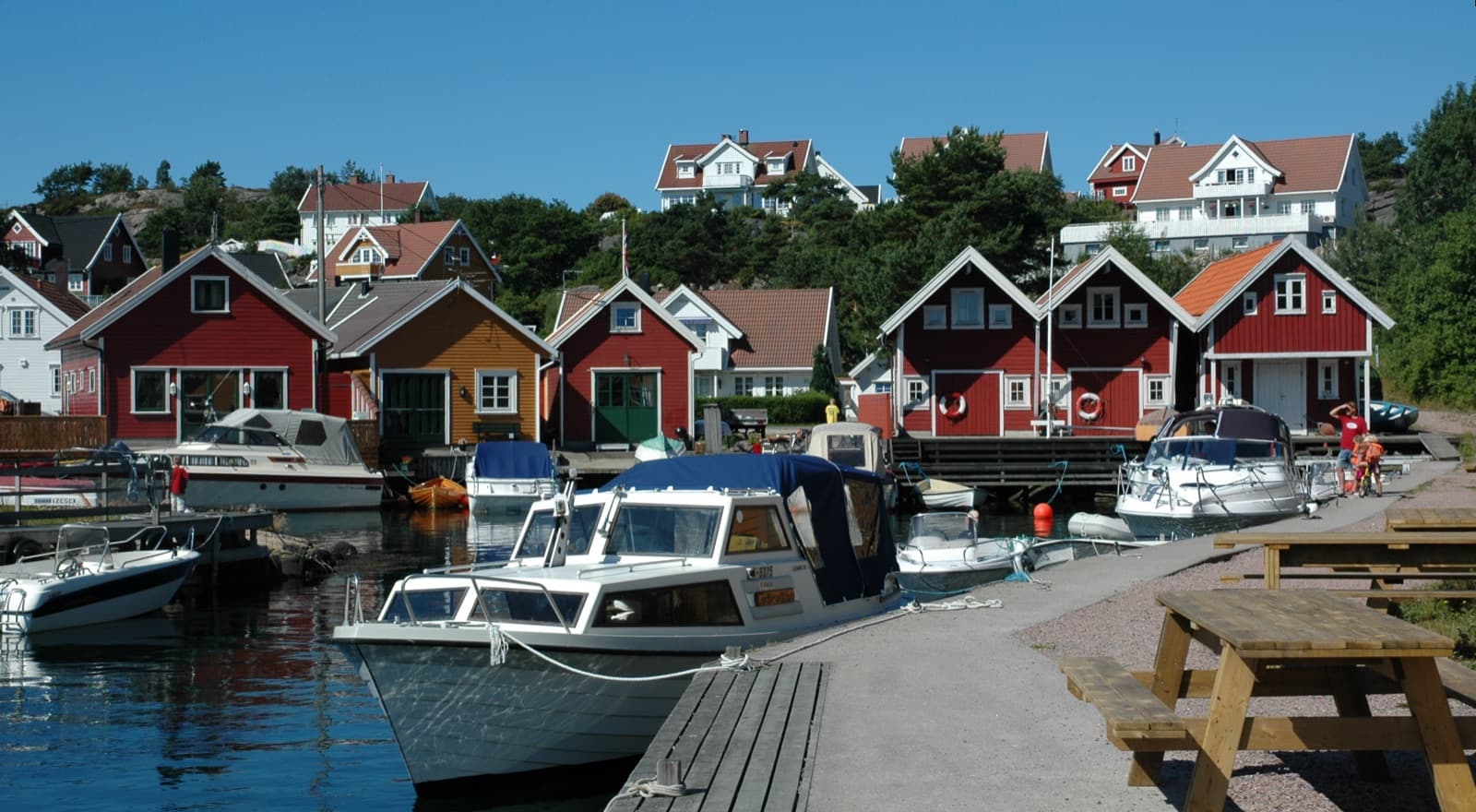 Red boathouses and moored boats in the Paulen inlet, with houses on the rocky slope behind, Flekkerøy, Kristiansand, Norway.