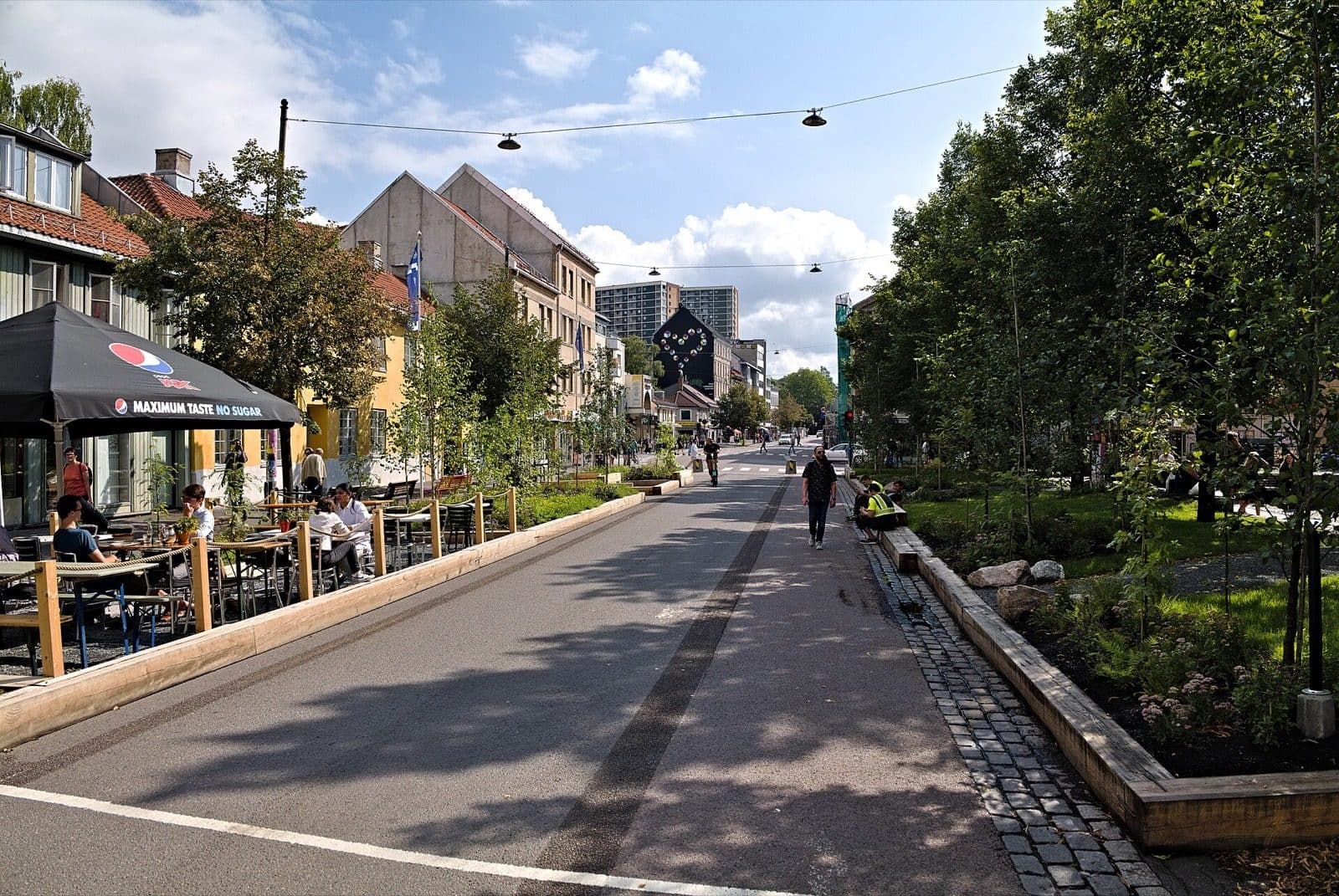 The Grønland street in Oslo on a summer afternoon, with cafe tables under parasols and new planting along the roadside.
