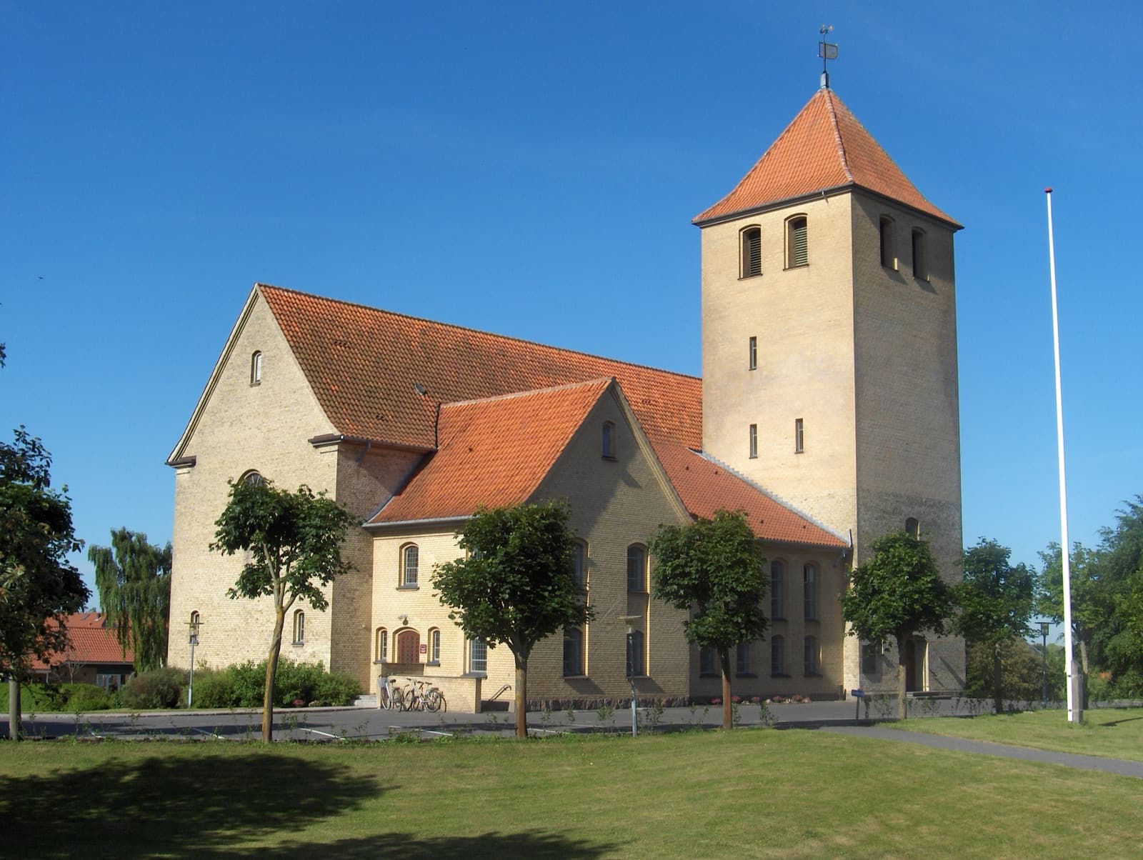 Hasseris Church, a yellow-brick church with a red-tiled roof and tower amid lawns and trees in the affluent Hasseris suburb of Aalborg, Denmark.