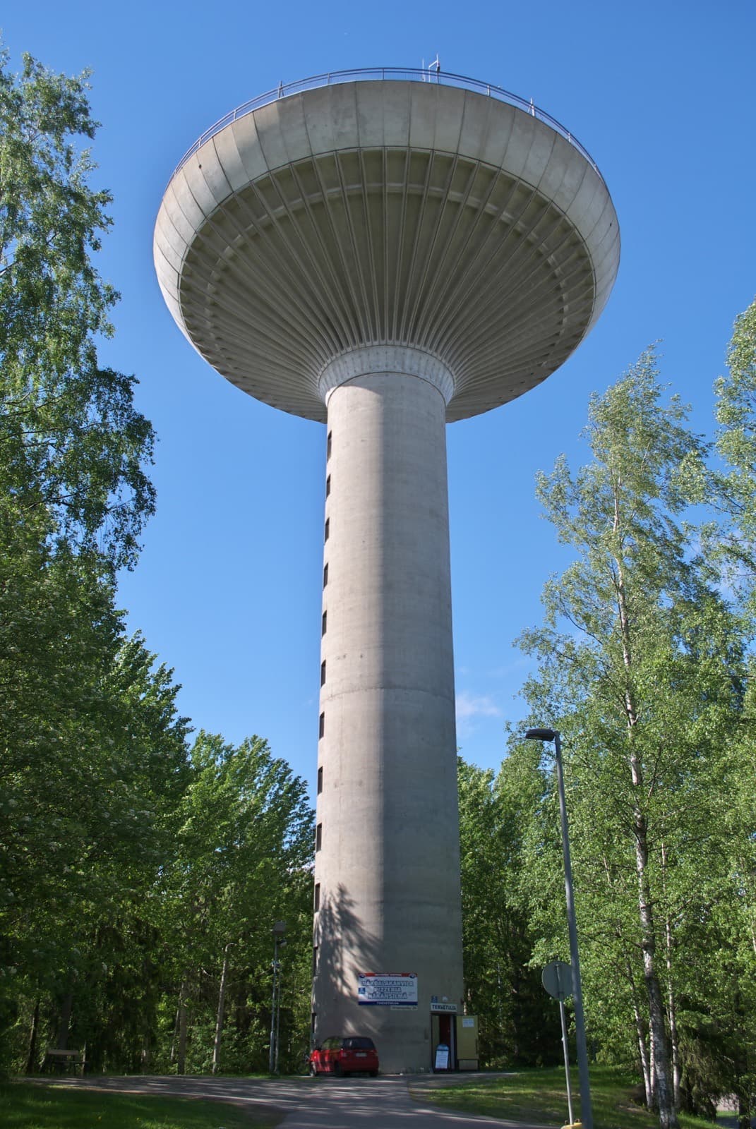 The mushroom-shaped concrete water tower of Hervanta, Tampere, rising above the birches against a clear blue sky.