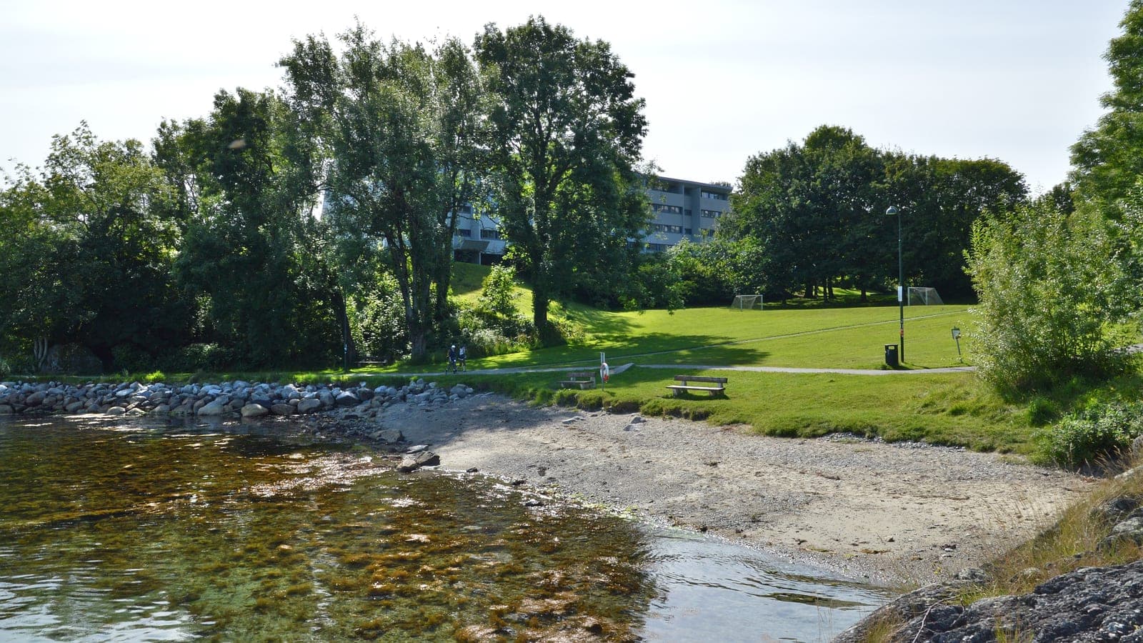 The shore and lawns at Rosenli, with apartment blocks set back among the trees, in Hillevag, Stavanger.