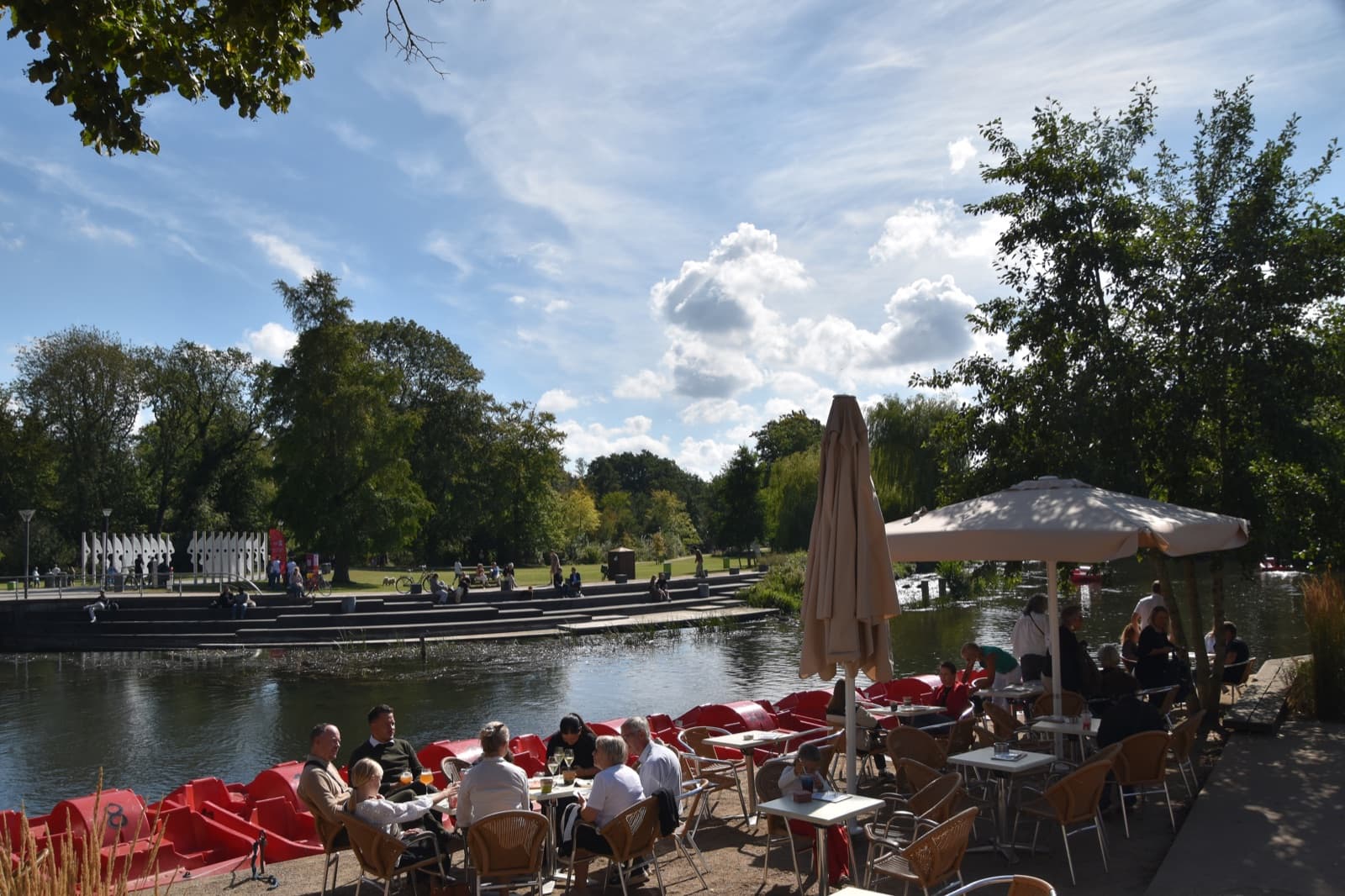 A riverside cafe terrace and red pedal boats on the Odense river at Munke Mose park, beside the Hunderup villa district of Odense.