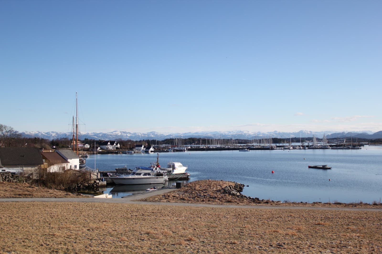 Boats moored in a sheltered bay on Hundvåg with the snow-capped Ryfylke mountains across the water, Hundvåg, Stavanger, Norway.