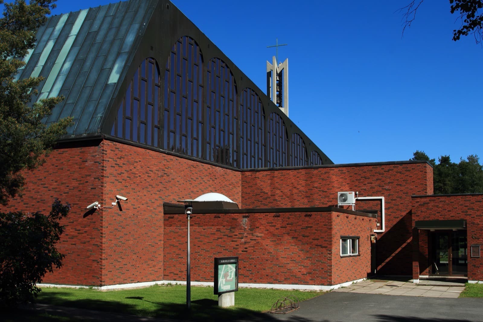 The red-brick Karjasilta Church and its free-standing bell tower in Karjasilta, Oulu, on a summer day.