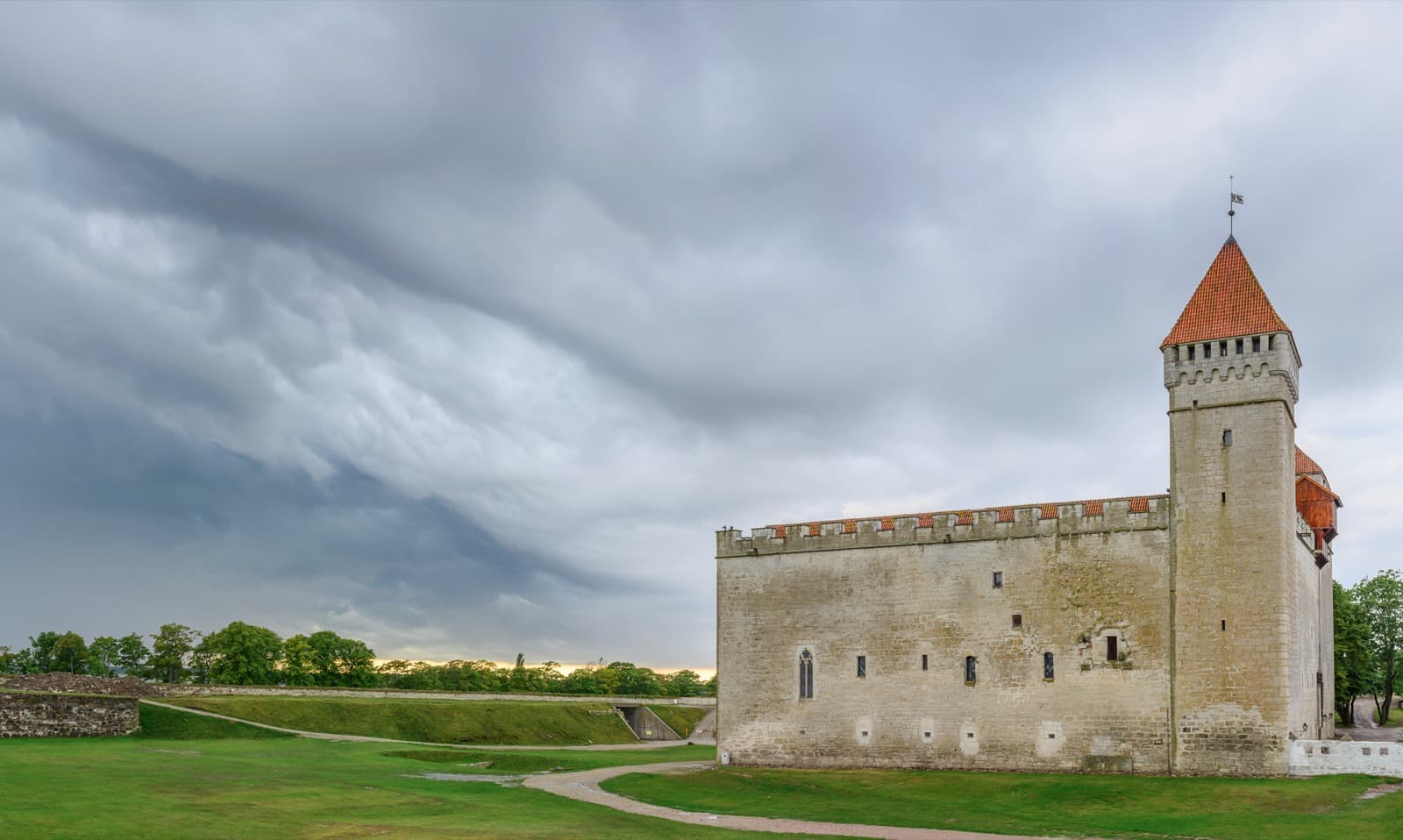 Kuressaare Castle, the medieval bishop's castle with its red-roofed tower and stone keep, on a green lawn under a dramatic sky.