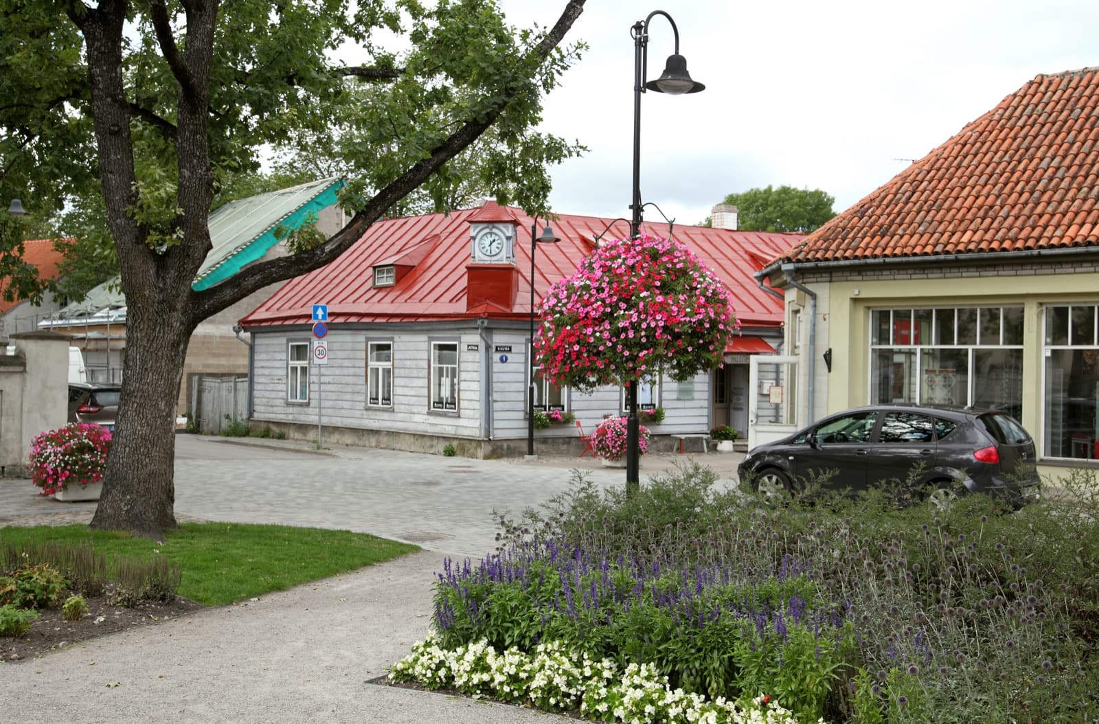 A wooden red-roofed old-town house with a street clock and summer flower baskets on a cobbled corner in central Kuressaare.