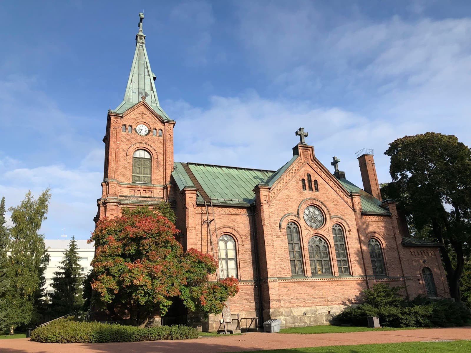 The red-brick Jyväskylä city church in its park in the centre of Jyväskylä, with a rowan turning red beside the clock tower.