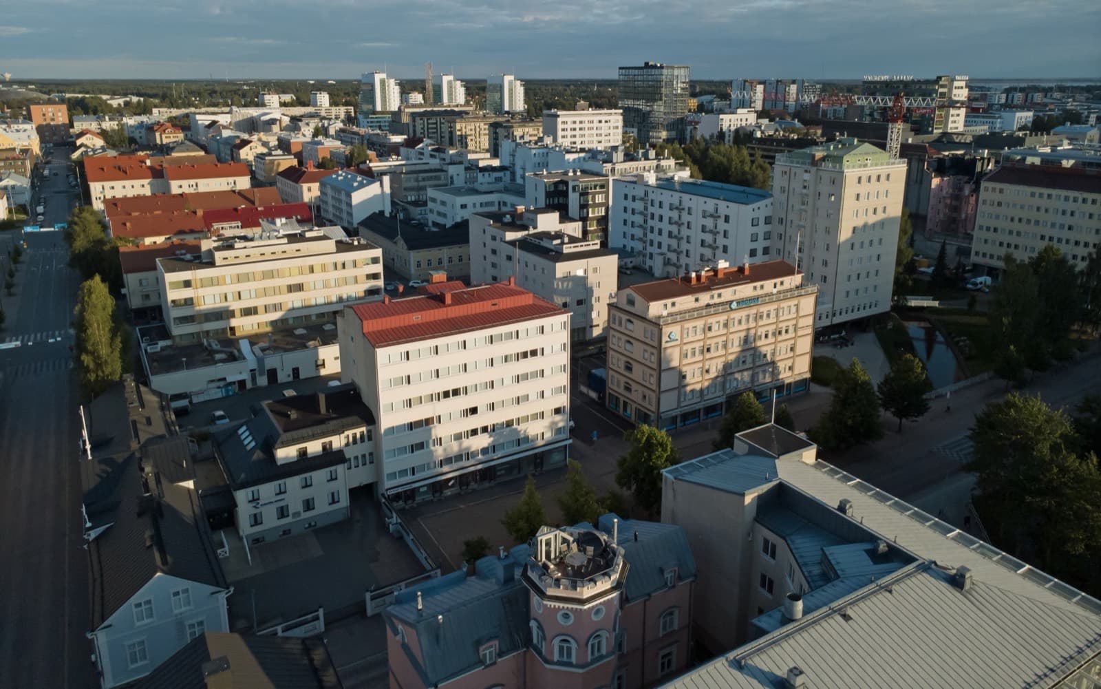 The dense downtown blocks of central Oulu in low evening light, seen from above with the sea on the horizon.