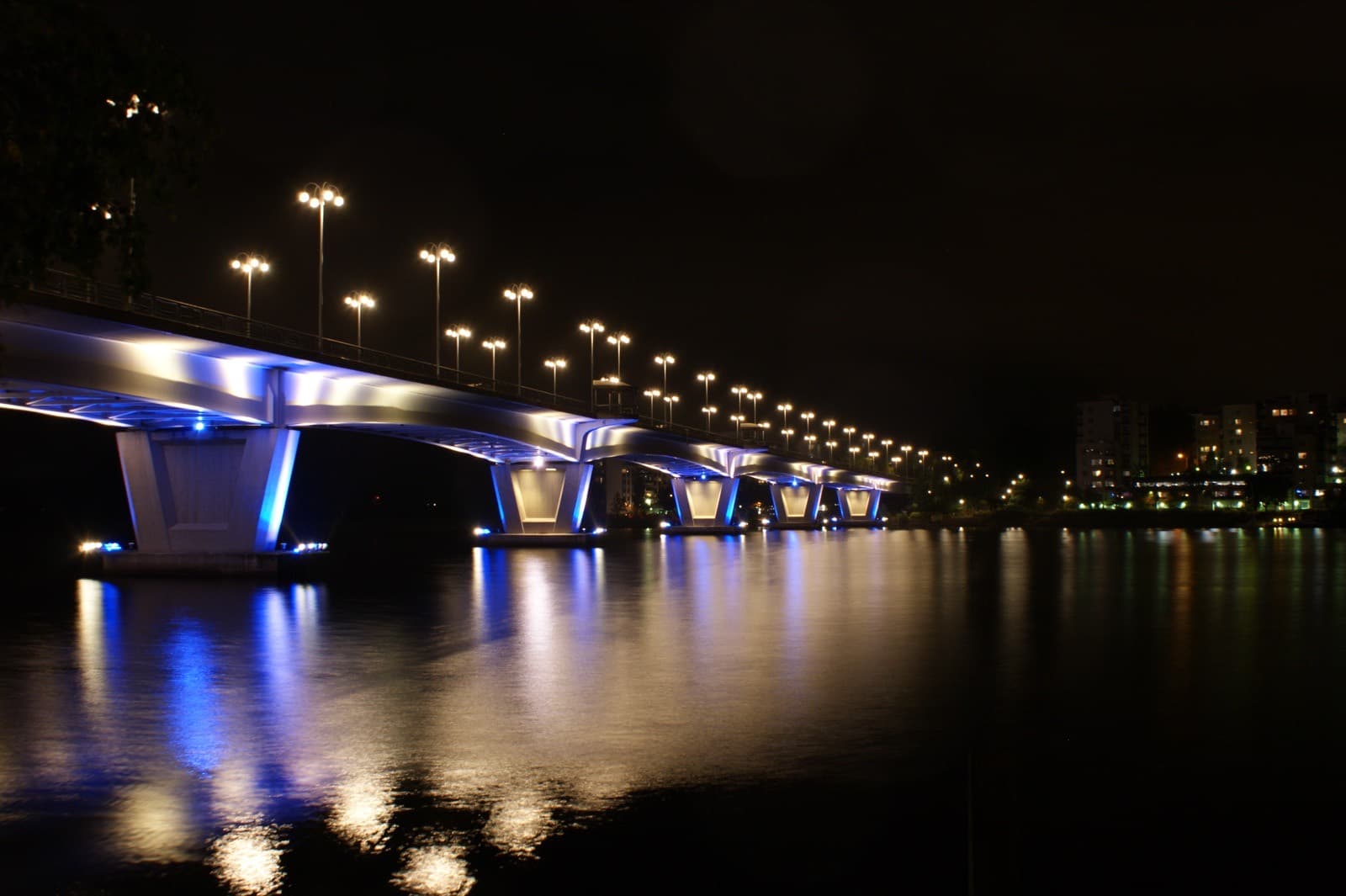 The Kuokkala bridge lit blue at night over Lake Jyväsjärvi in Jyväskylä, with the lights of Kuokkala along the far shore.