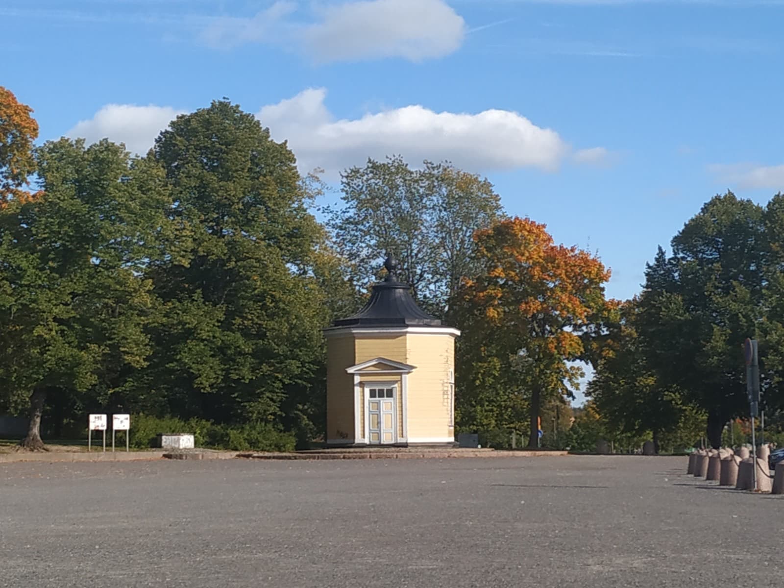 The yellow Piispanlähde spring pavilion among autumn trees in Kupittaa Park, Turku, under a blue sky.