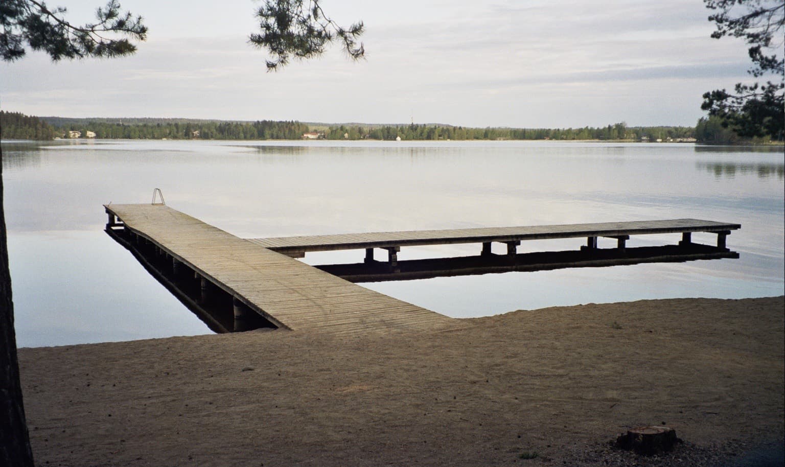 A wooden jetty on the still water of Lake Näsijärvi at Suomensaari beach in Lentävänniemi, Tampere, early on a spring morning.