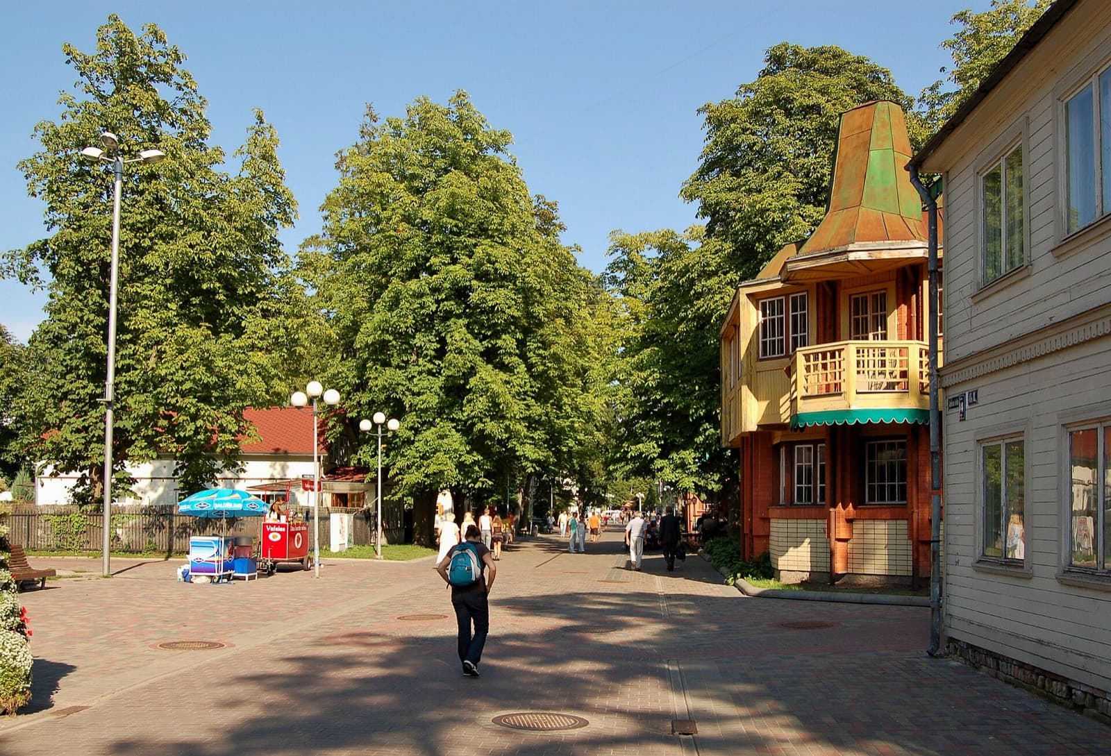 The pedestrian Jomas iela in Majori on a summer day, tree-lined and passing a wooden resort villa with a corner turret, Jūrmala, Latvia.