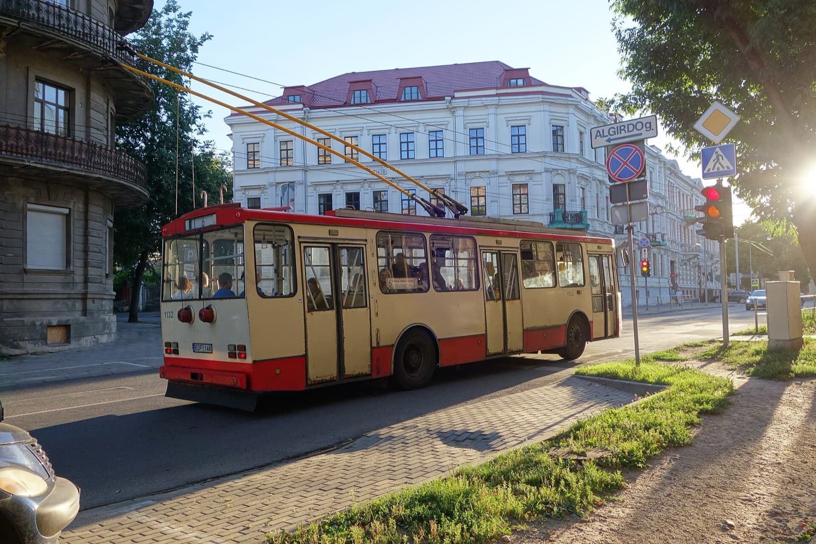 A vintage trolleybus on Algirdo street in Naujamiestis, passing a grand interwar apartment building in warm evening light.