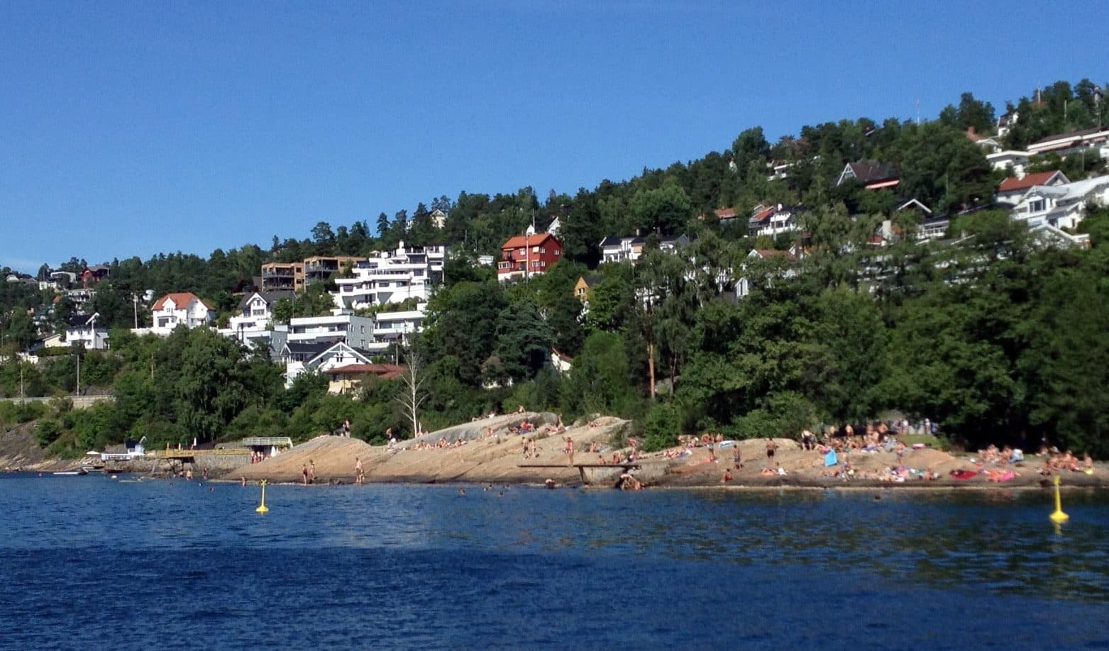 The Katten bathing rocks on the Oslofjord below Nordstrand, with the wooded villa hillside rising behind.