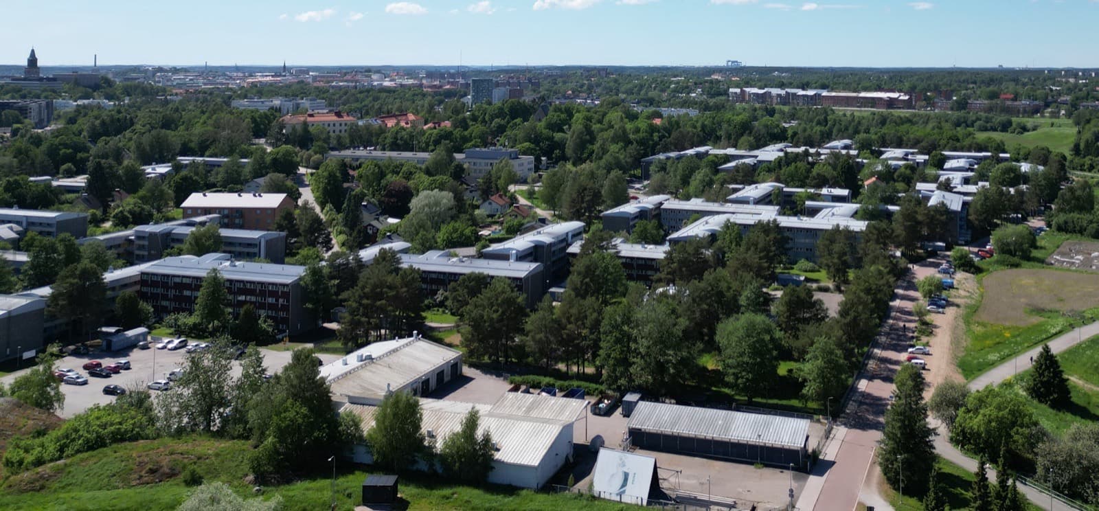 The low blocks and pine-lined courtyards of the Turku Student Village in Nummi, seen from the air with the city and the cathedral tower beyond.