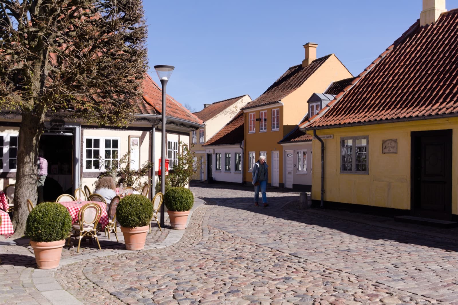A cobbled square lined with yellow half-timbered cottages and cafe tables in the H.C. Andersen quarter of central Odense.