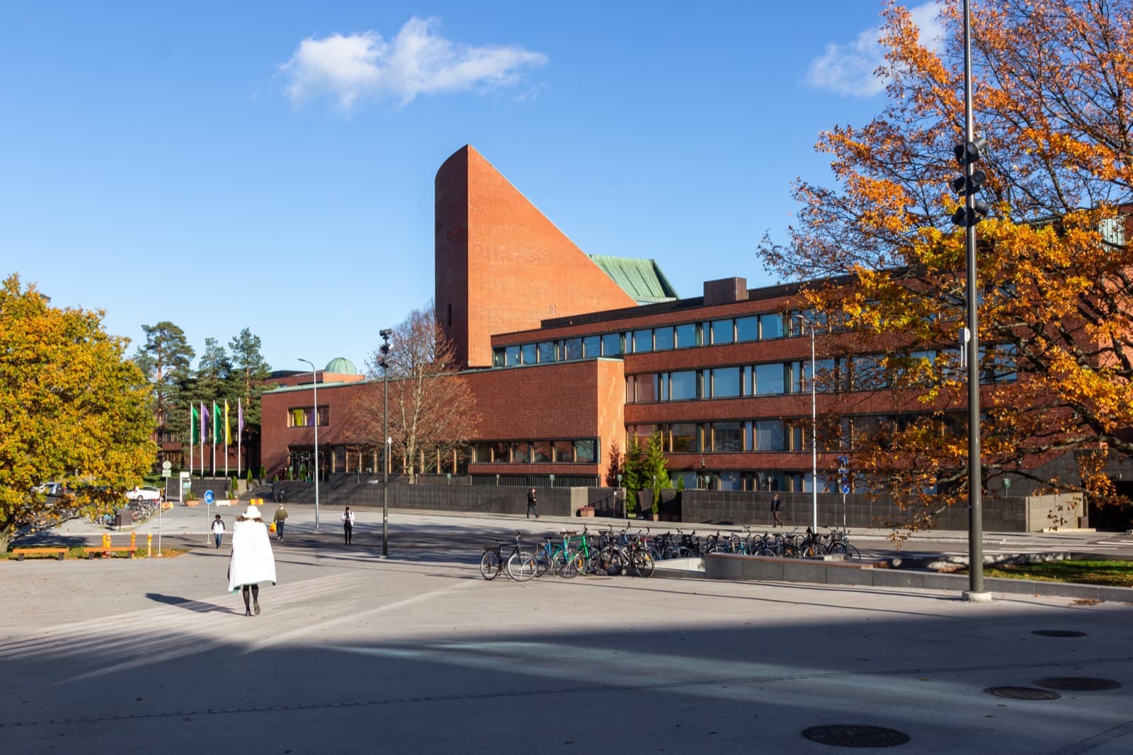 Alvar Aalto's red brick main building in Otaniemi, Espoo, with its fan-shaped auditorium rising above the campus square on a clear autumn day.