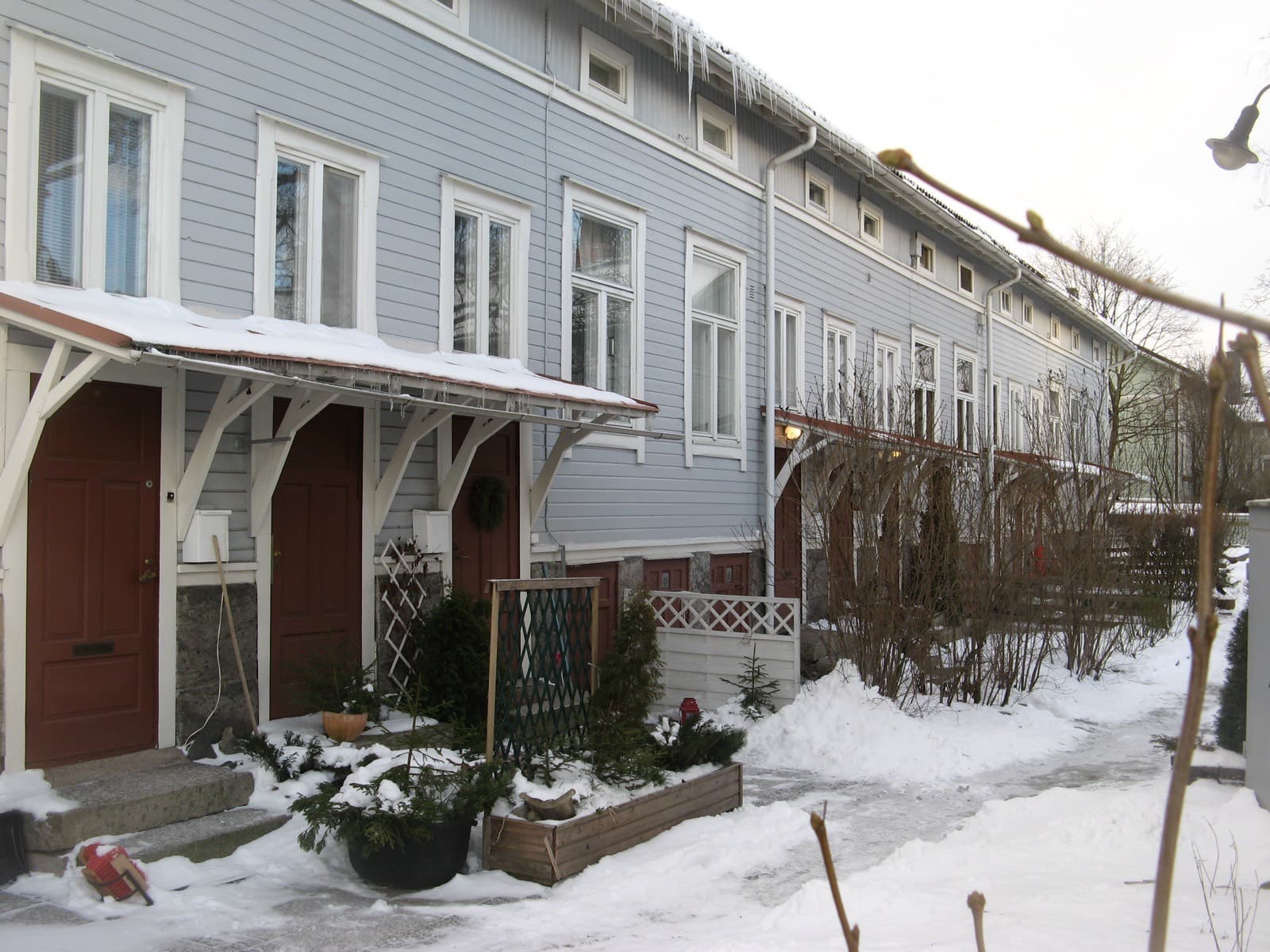 A pale blue wooden terrace with red doors and small front gardens on a snowy lane in Port Arthur, Turku.