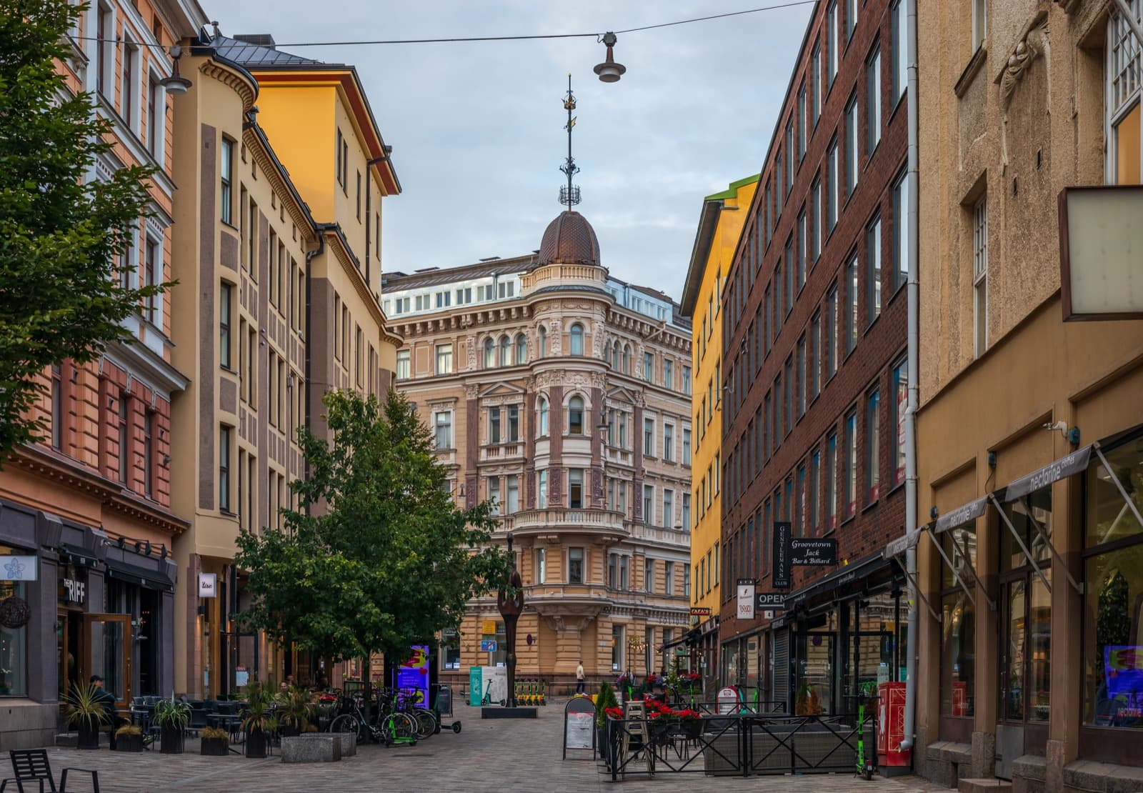 The pedestrianised Iso Roobertinkatu in Punavuori, Helsinki, lined with café terraces and small shops, closed at the end by an ornate domed corner building.