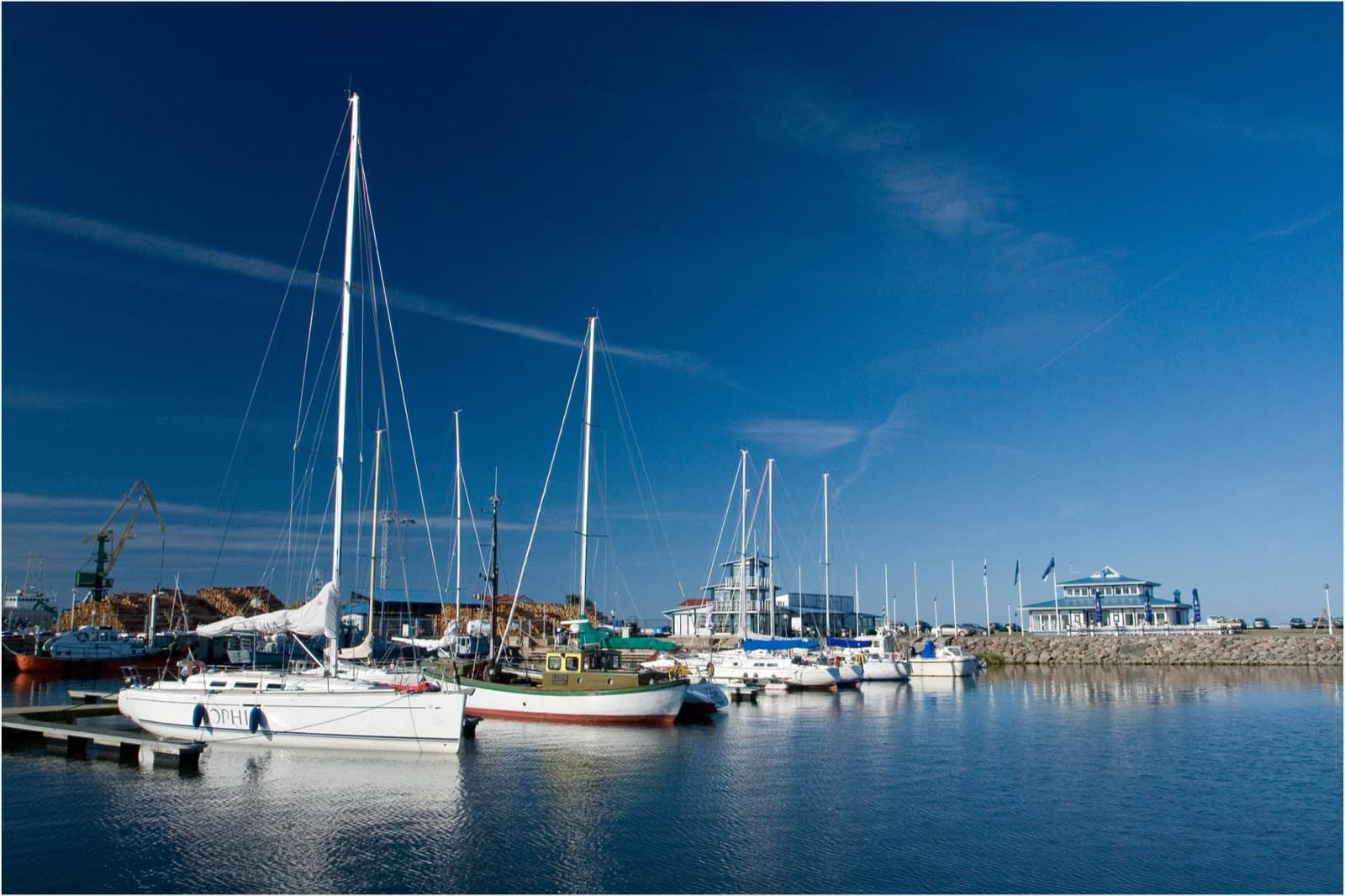 Sailboats and small craft moored at Roomassaare yacht marina under a clear blue sky, with the harbour buildings beyond.