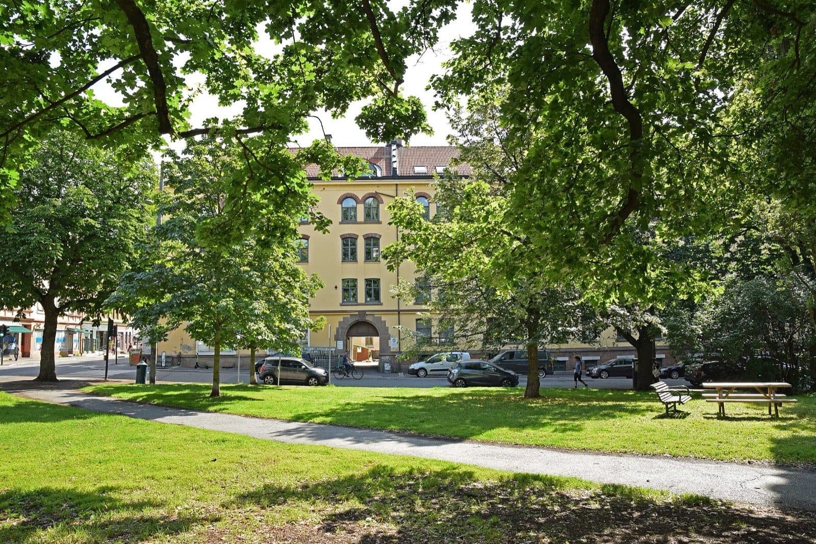Sagene kirkepark in Oslo in summer, with mature trees, a picnic table and the apartment blocks of Grimstadgata behind.