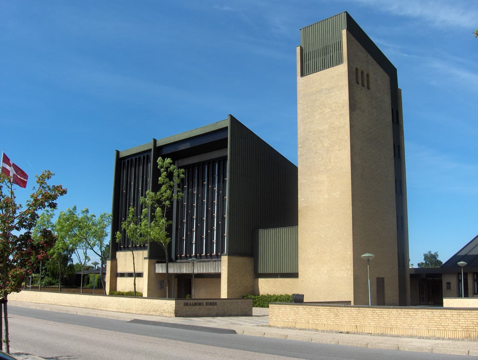Skalborg Church, a modern brick church with an angular facade and tall tower under a blue sky, in the Skalborg suburb south-west of Aalborg, Denmark.