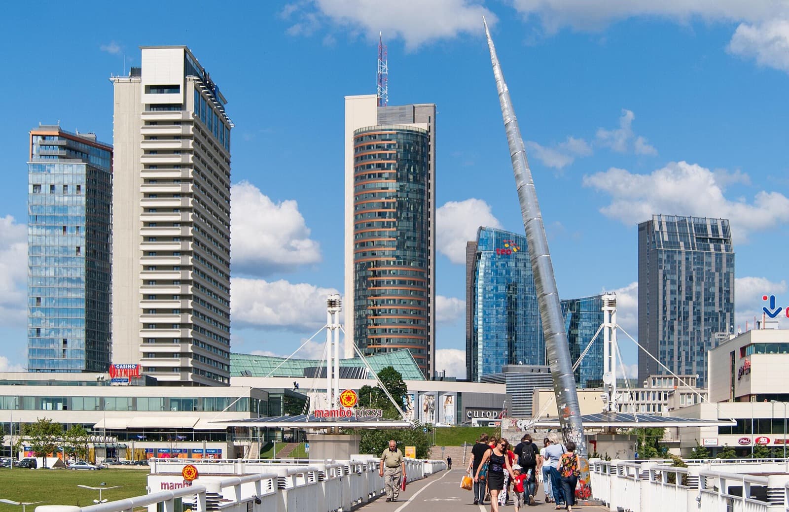 The glass office towers of the Snipiskes business district seen from the White Bridge over the Neris under a summer sky.