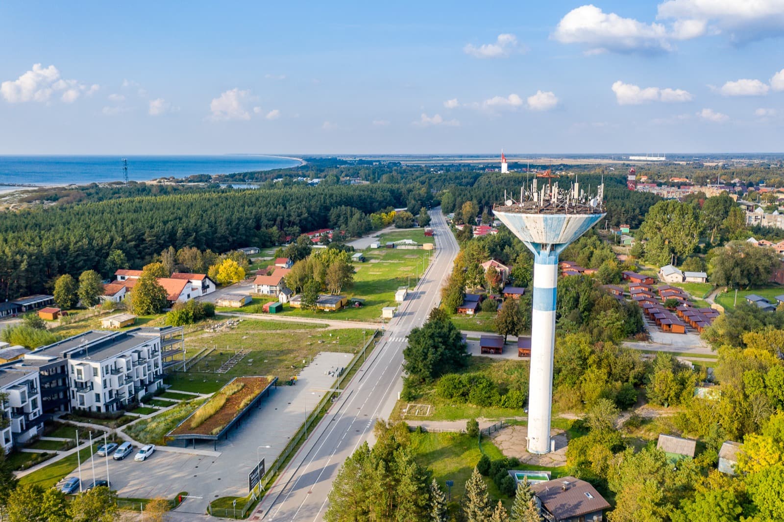 Aerial view of the low-rise Šventoji seaside resort, its striped water tower rising above pine forest with the Baltic coast beyond