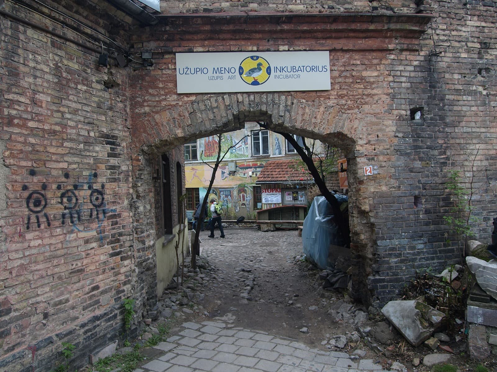 The brick gateway of the Uzupis Art Incubator opening onto a muralled bohemian courtyard in Uzupis.