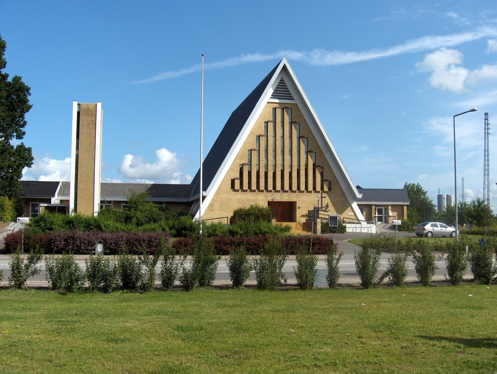 Vesterkær Church, a striking A-frame modern church in yellow brick with a green lawn in front, in the Vestbyen district west of central Aalborg, Denmark.