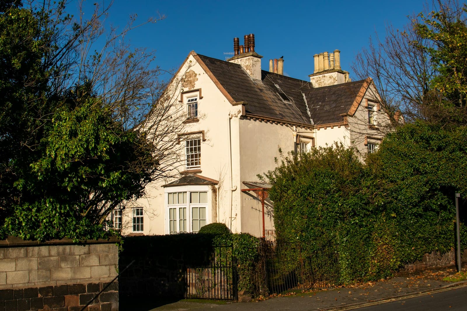 A detached period house behind hedges and a mature garden on a quiet street