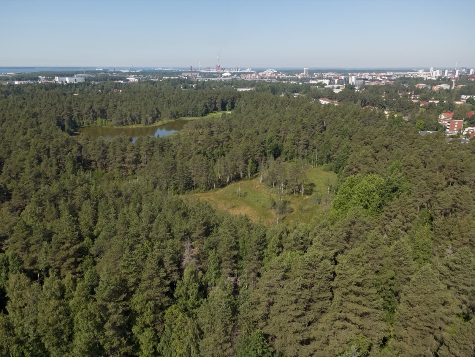 The pine woods and pond of Lintulammenpuisto park in Höyhtyä, Oulu, seen from the air with the city beyond.