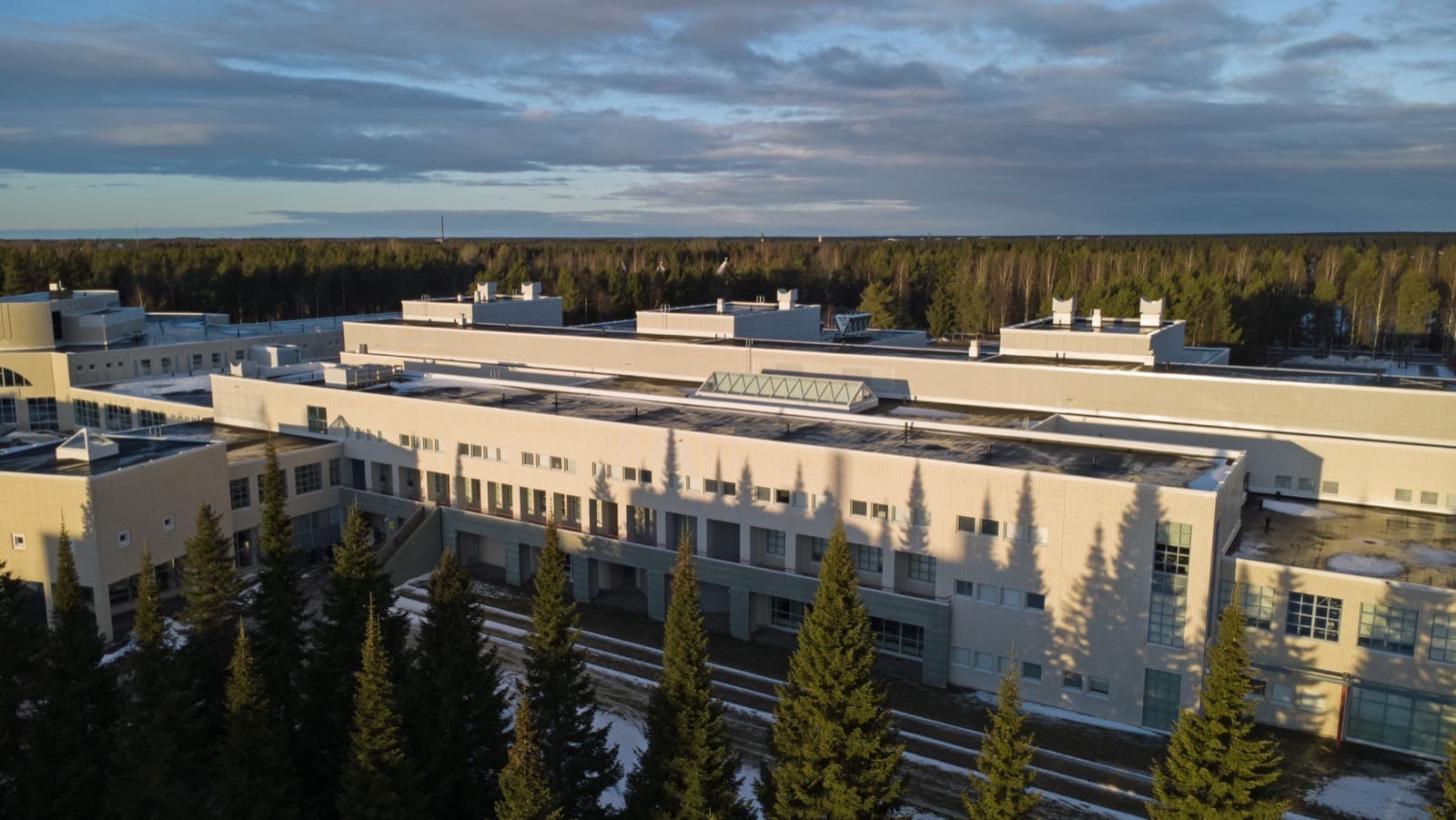 The long low buildings of the University of Oulu's Linnanmaa campus in winter light, backed by pine forest.