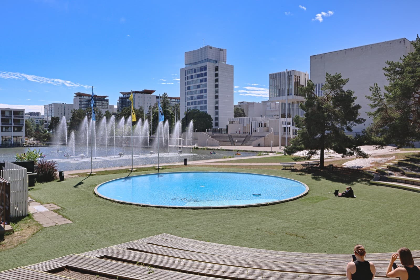 The central pool and fountains of Tapiola in Espoo on a summer day, with lawns, pines and the white modernist towers of the garden city behind.