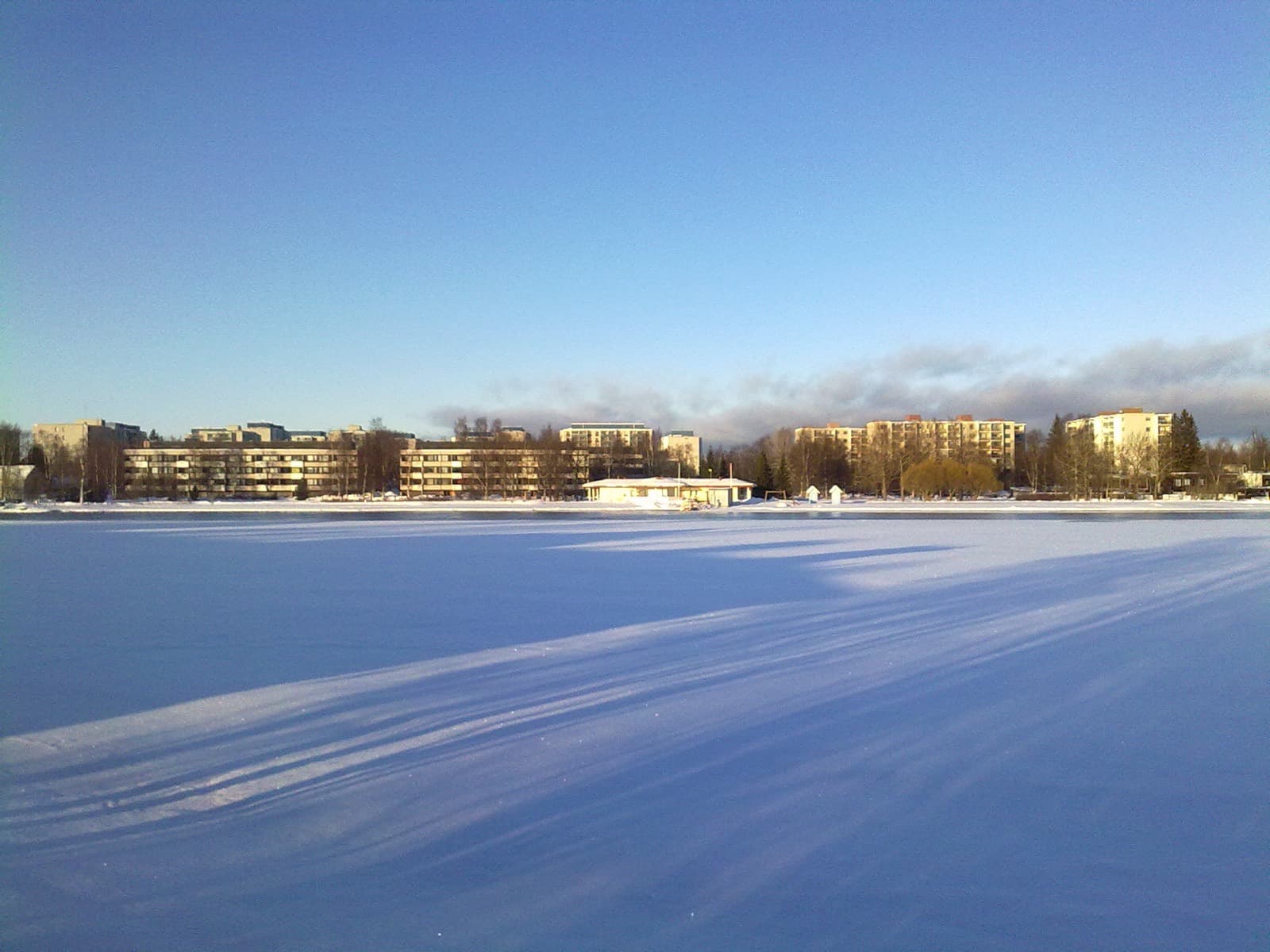 The frozen Oulujoki at Tuira beach in Oulu on a bright winter day, with the apartment blocks of Tuira lining the far bank.